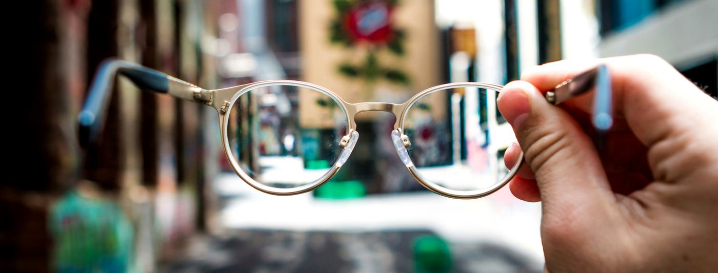 Spectacles held up, the street sharp through the lens