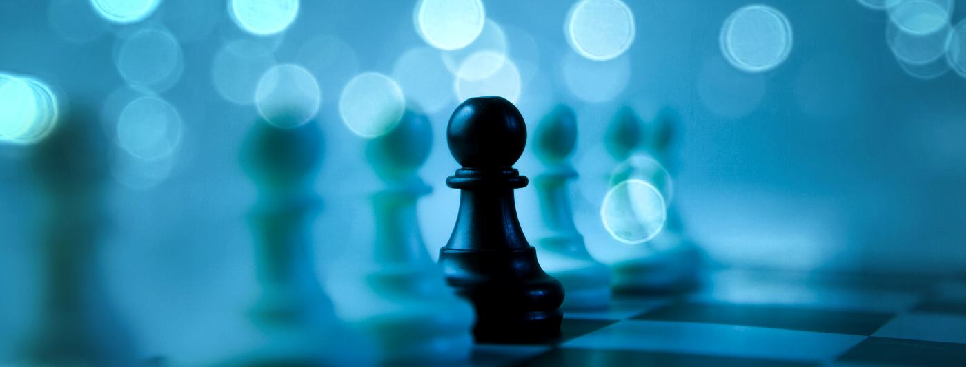 A single dark chess piece among blurred pieces