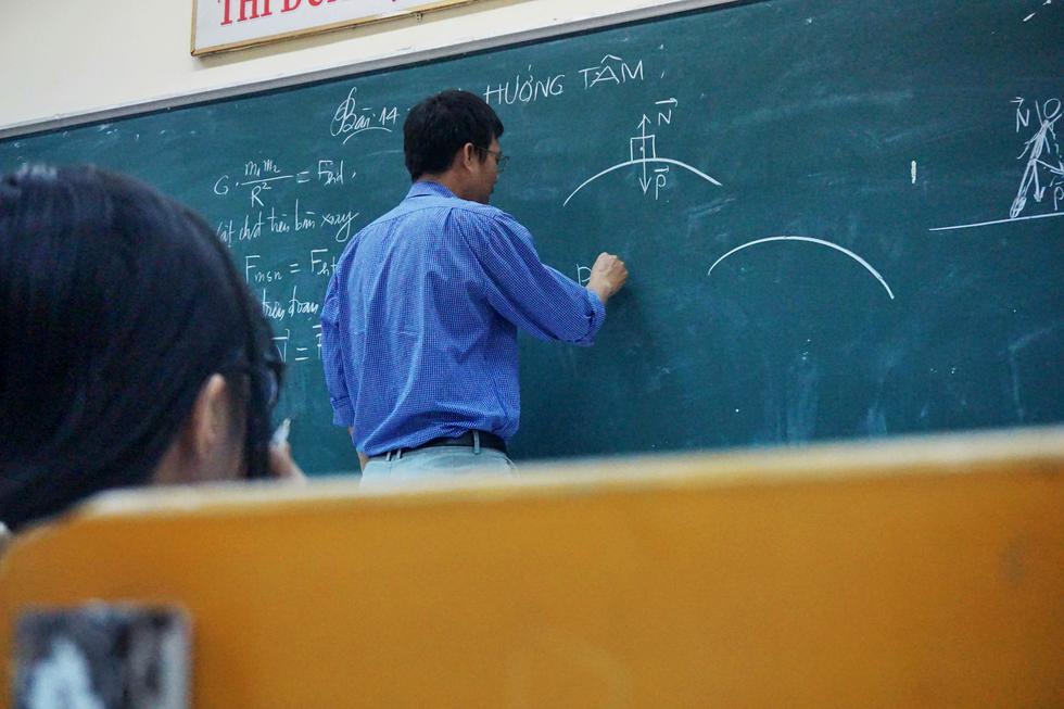 A teacher writing at a blackboard, seen from the back of the room