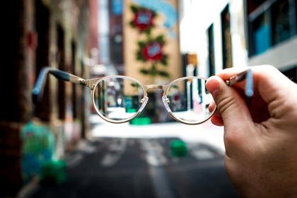 Spectacles held up, the street sharp through the lens